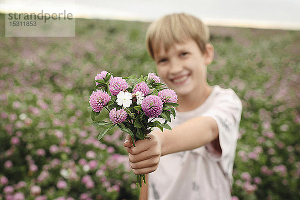 Lächelnder Junge schenkt Kleeblumen