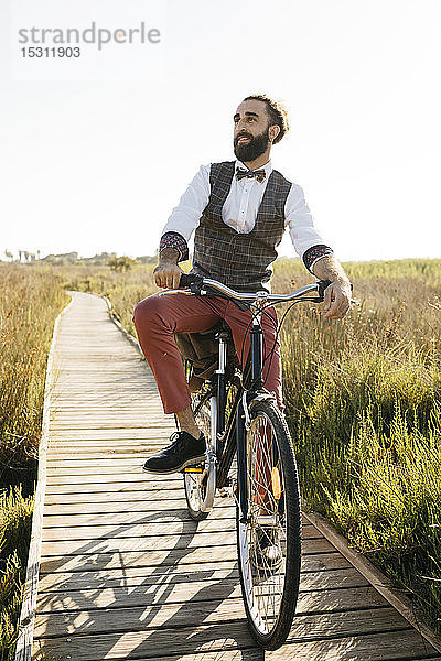 Gut gekleideter Mann mit seinem Fahrrad auf einem Holzsteg auf dem Land  der eine Pause macht