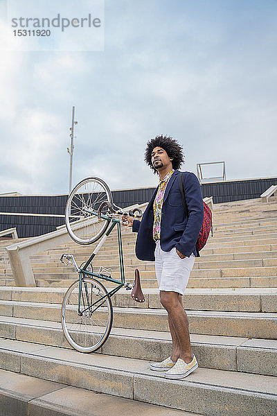 Stilvoller Mann mit Fahrrad auf der Treppe in der Stadt