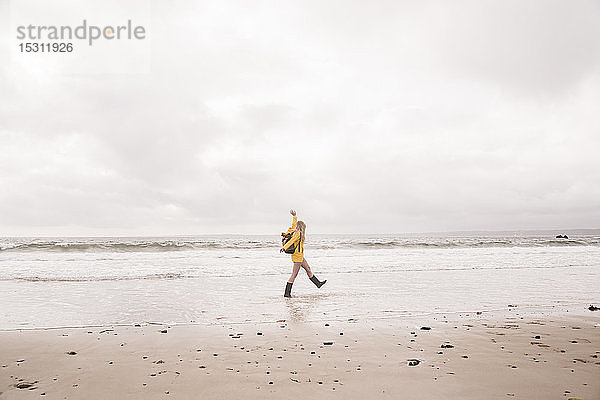 Frau mit gelber Regenjacke geht am Strand spazieren