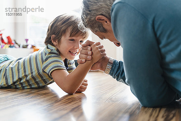 Vater und Sohn liegen zu Hause auf dem Boden und machen Armdrücken