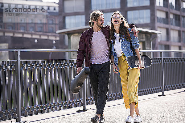 Glückliches junges Paar mit Skateboard auf einer Brücke