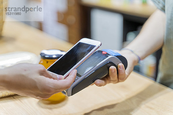 Kunden  die in einem Geschäft bargeldlos mit einem Smartphone bezahlen