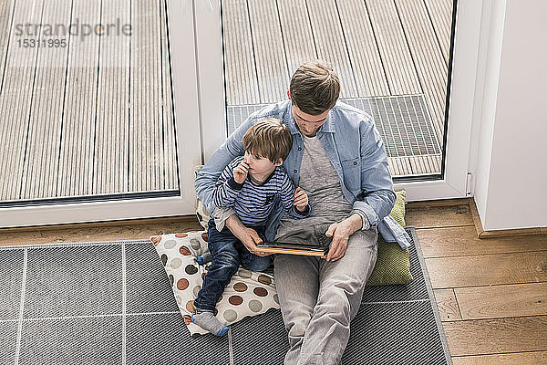 Vater und Sohn sitzen auf dem Boden und benutzen ein digitales Tablett