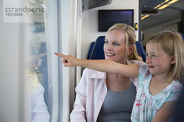 Mutter und Tochter reisen mit dem Zug und zeigen aus dem Fenster