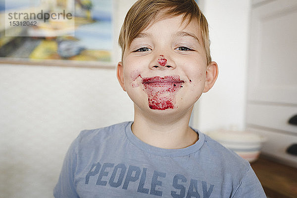 Porträt eines grinsenden Jungen mit Heidelbeermarmelade im Gesicht