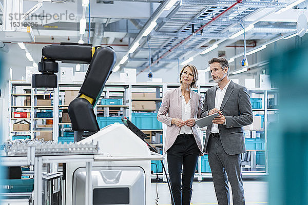 Geschäftsmann und Geschäftsfrau in einer modernen Fabrikhalle mit Blick auf Roboter