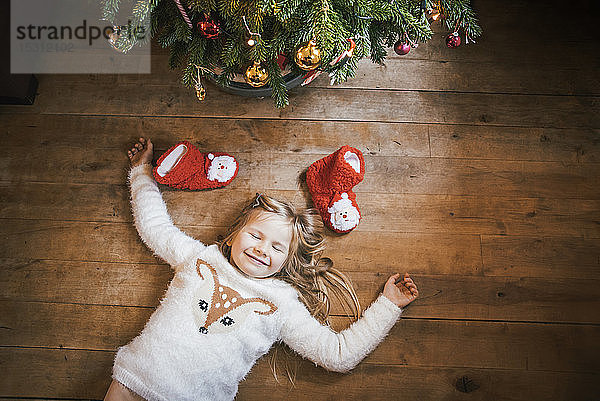 Lächelndes Mädchen mit geschlossenen Augen unter dem Weihnachtsbaum liegend