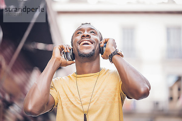 Porträt eines glücklichen Mannes  der mit Kopfhörern Musik hört und nach oben schaut
