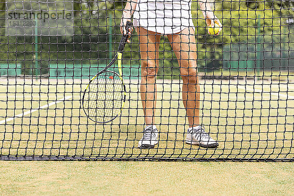 Beine der Tennisspielerin auf Rasenplatz durch das Netz gesehen