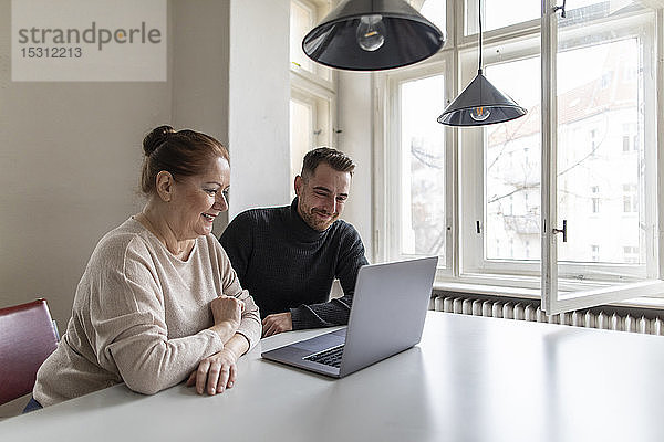 Lächelnde ältere Frau und Mann schauen auf den Laptop auf dem Tisch