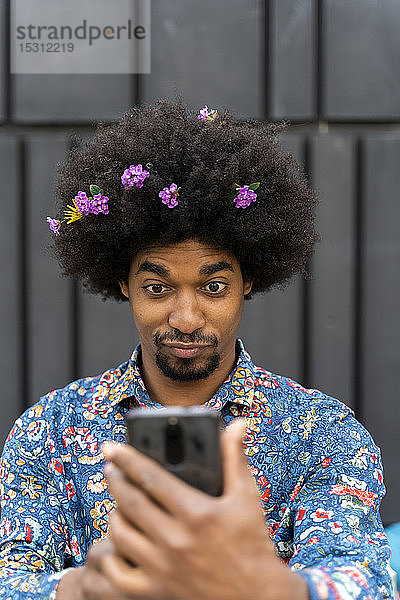 Mann mit Blüten im Haar trägt buntes Hemd und nimmt ein Selfie