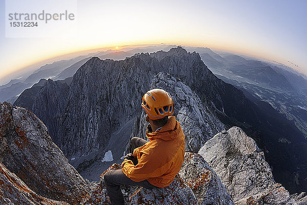 Bergsteiger mit orangem Helm sitzt bei Sonnenaufgang auf dem Ellmauer Halt  Wilder Kaiser  Ellmauer Halt  Tirol  Österreich