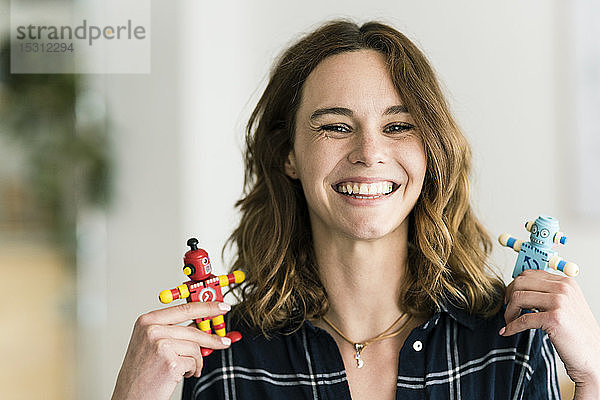 Lachende Frau hält männliche und weibliche Spielzeugroboter