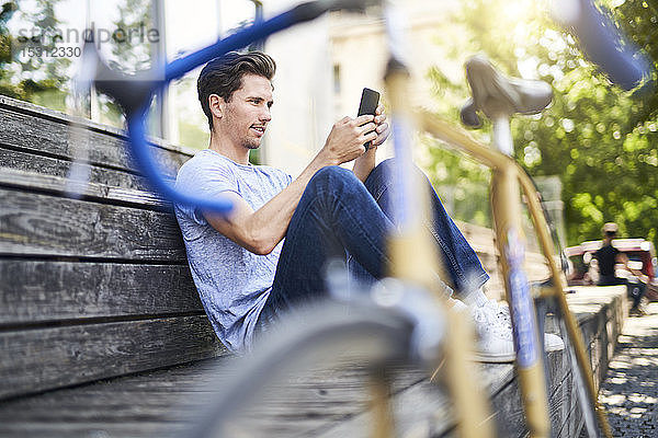 Mann mit Rennrad auf Bank sitzend mit Smartphone
