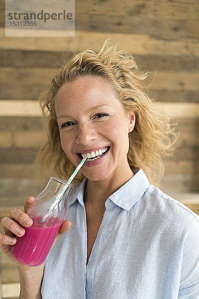 Lächelnde blonde Frau trinkt einen Smoothie