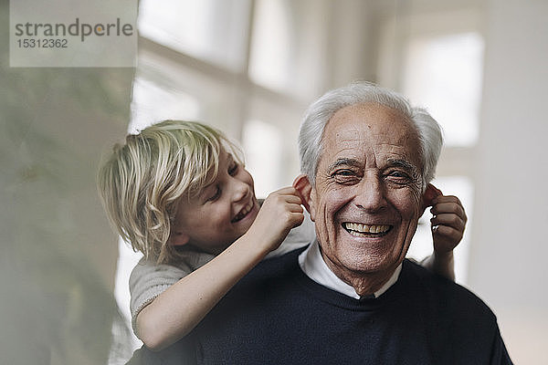 Glücklicher Enkel zieht zu Hause am Großvater an den Ohren