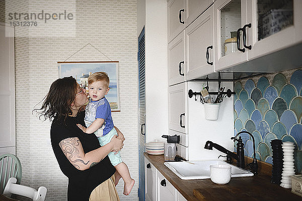 Mutter trägt ihren kleinen süßen Sohn in der Küche