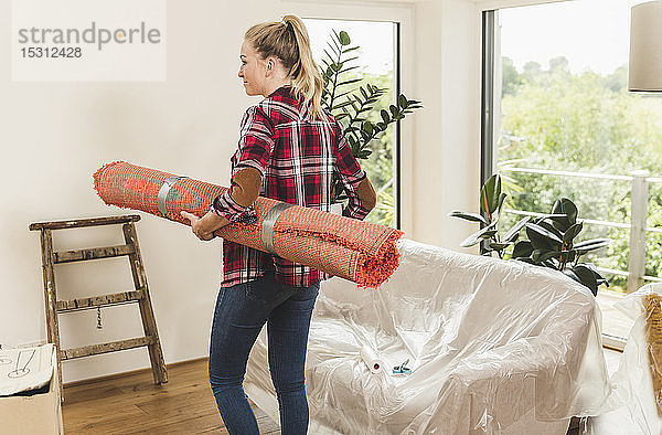 Rückansicht einer Frau  die mit Teppich und Topfpflanze in ihr neues Zuhause einzieht