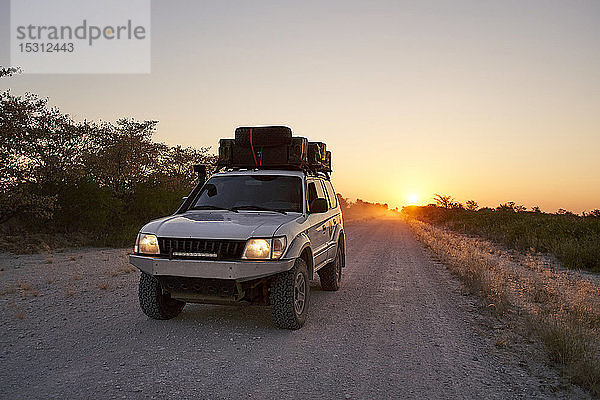 Geländewagen fährt bei Sonnenaufgang auf einer unbefestigten Straße  Makgadikgadi Pans  Botswana