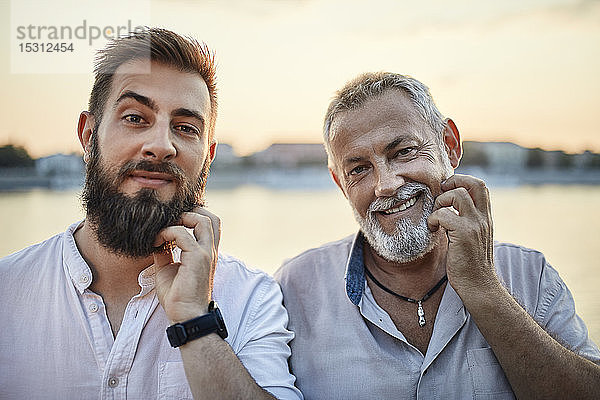 Porträt eines lächelnden Vaters und eines erwachsenen Sohnes  die sich am Bart kratzen