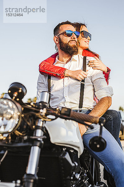 Porträt eines Paares  das in der Abenddämmerung auf einem Motorrad sitzt und in die Ferne schaut