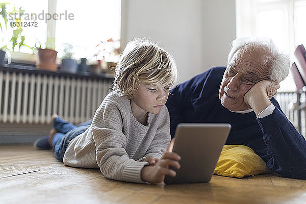 Großvater und Enkel liegen zu Hause mit einer Tablette auf dem Boden