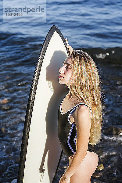 Weiblicher Teenager mit Surfbrett am steinigen Strand