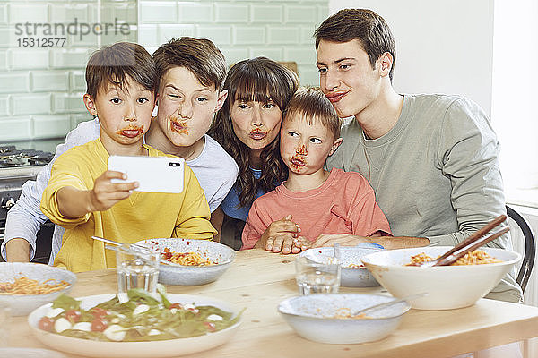 Mutter und ihre vier Söhne mit Smartphone-Selbstfahrern beim Mittagessen  mit Gesichtern voller Tomatensauce