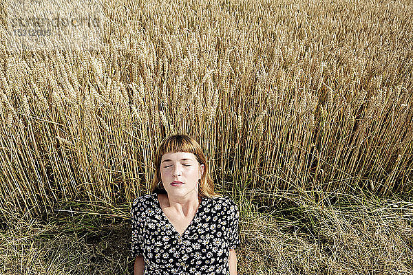 Bildnis einer jungen Frau mit geschlossenen Augen  die sich vor einem Kornfeld entspannt