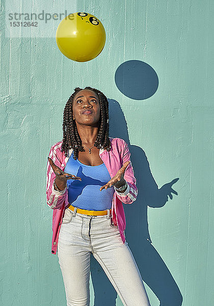 Junge schwarze Frau spielt mit einem farbigen Ball vor einer blauen Wand