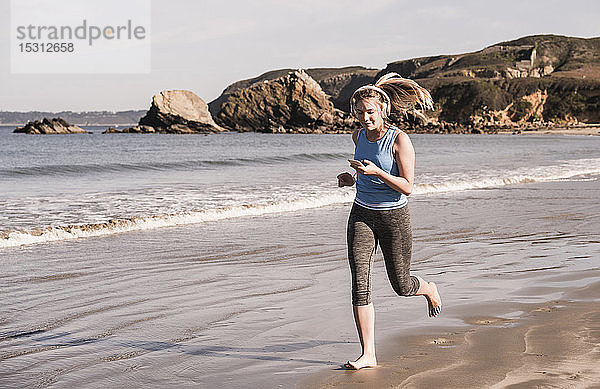 Joggerin am Strand  mit Smartphone und Kopfhörern