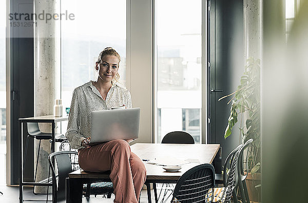 Porträt einer Geschäftsfrau  die mit Laptop auf einem Tisch im Büro sitzt