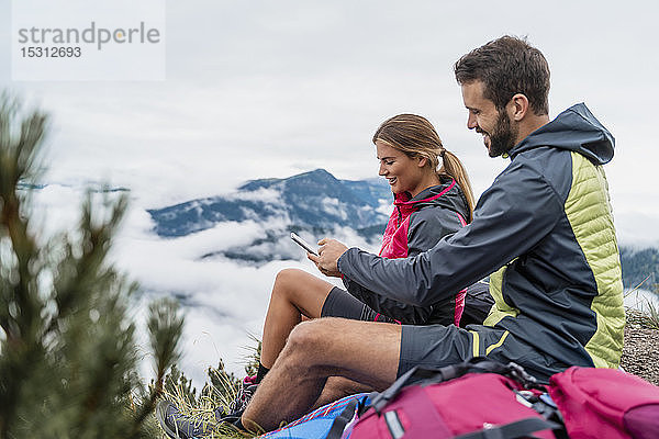 Junges Paar auf einer Wanderung in den Bergen macht eine Pause mit dem Handy  Herzogstand  Bayern  Deutschland