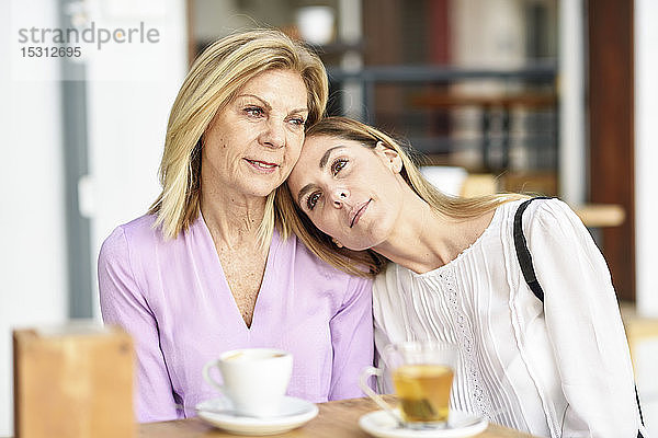 Eine reife Frau mit ihrer Tochter sitzt an einem Tisch im Freien in einem Café