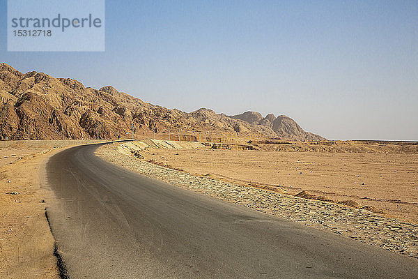 Leere Straße durch eine Felsformation in der Wüste bei strahlend blauem Himmel