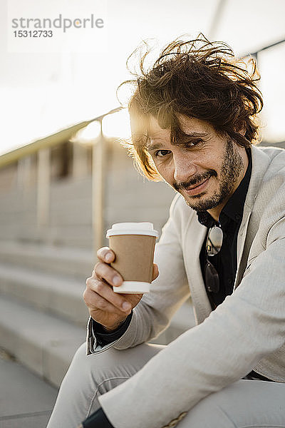 Porträt eines Geschäftsmannes mit Kaffee zum Mitnehmen im Gegenlicht auf einer Treppe sitzend