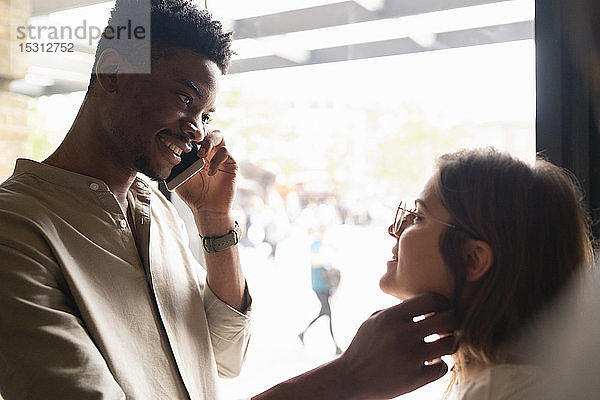 Porträt eines lächelnden jungen Mannes am Telefon  der seine Freundin berührt
