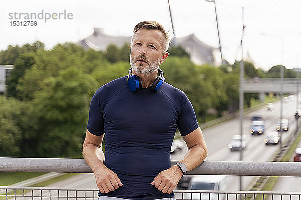 Sportlicher Mann mit Kopfhörern auf einer Brücke stehend