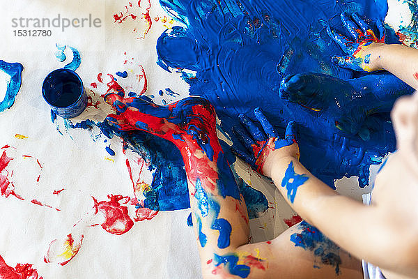 Kleinkind Mädchen sitzt auf Papier auf dem Boden und spielt mit Fingerfarben  Teilansicht