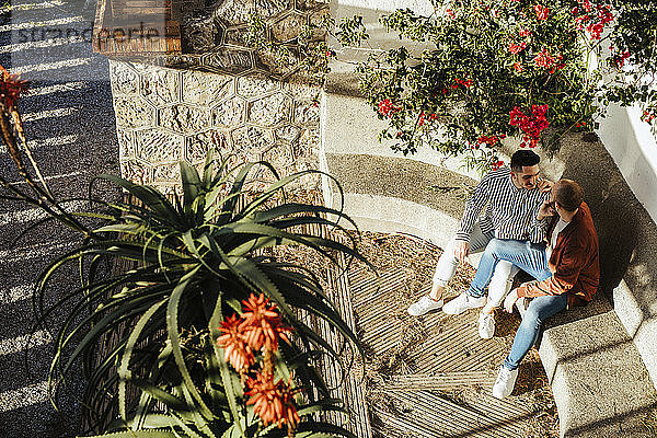 Homosexuelles Paar sitzt auf einer Stufe im Freien  umgeben von Blumen