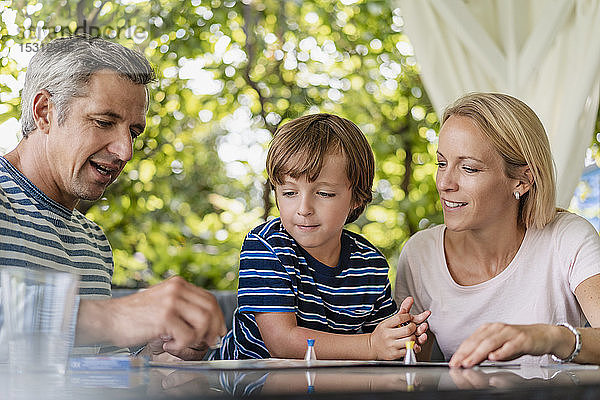 Glückliche Eltern und Sohn spielen ein Brettspiel auf der Terrasse