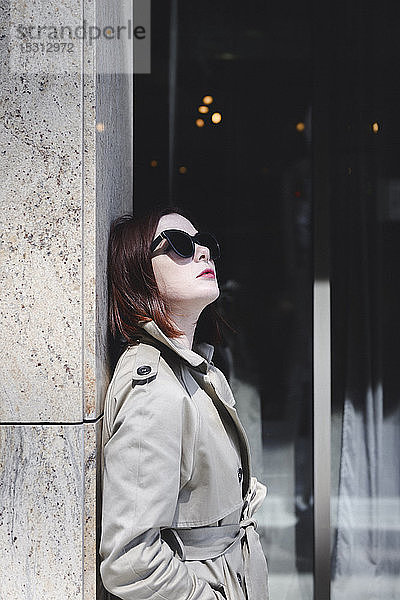 Porträt einer stilvollen Frau mit Sonnenbrille und Trenchcoat