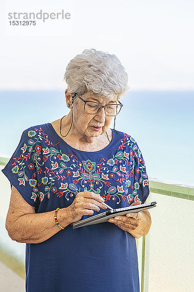 Ältere Frau benutzt eine Tablette auf einer Terrasse