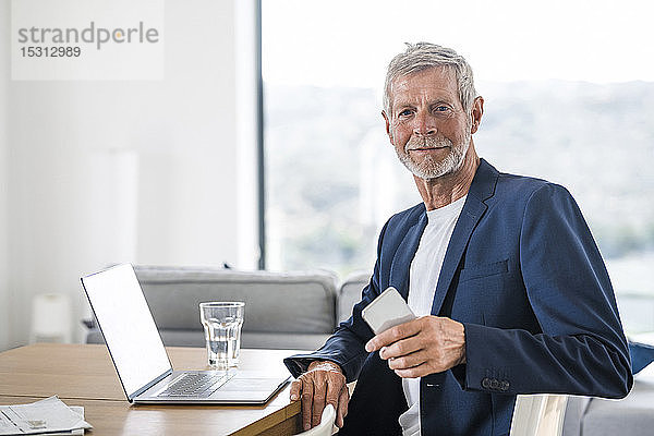 Porträt eines älteren Geschäftsmannes mit Laptop und Handy am heimischen Schreibtisch sitzend