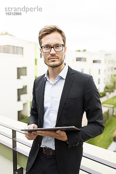 Porträt eines Geschäftsmannes mit Tablette auf einem Balkon in einem Neubaugebiet