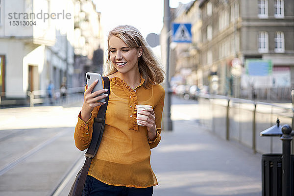 Lächelnde junge Frau mit Smartphone und Kaffee zum Mitnehmen in der Stadt