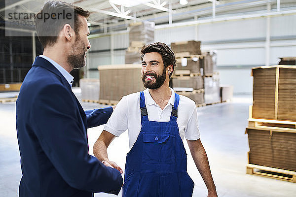 Geschäftsmann und Arbeiter beim Händeschütteln in einer Fabrik