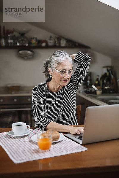Porträt einer älteren Frau mit Laptop am Frühstückstisch