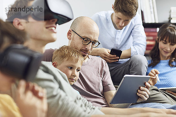 Glückliche Familie sitzt auf der Couch  benutzt VR-Brille und mobile Geräte